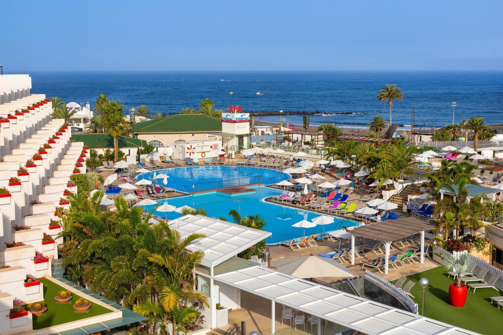 Alexandre Hotel Gala plašā teritorija ar āra baseiniem, saulessargiem un palmu dārzu pie okeāna krasta Tenerifē