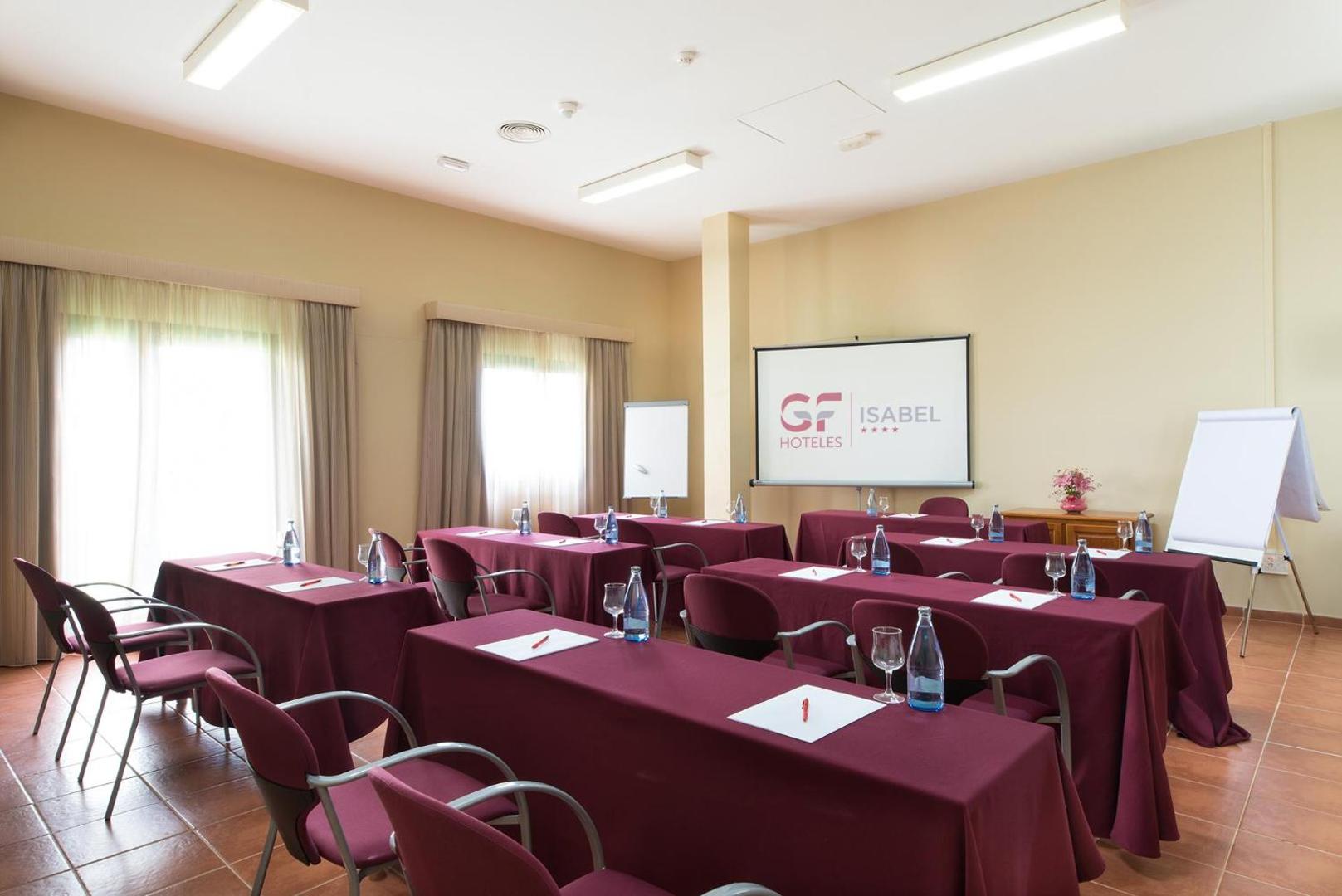 GF Isabel viesnīcas konferenču zāle ar galdiem, purpursarkaniem galdautiem, krēsliem un prezentāciju ekrānu darba pasākumiem Kostadeje, Tenerifē