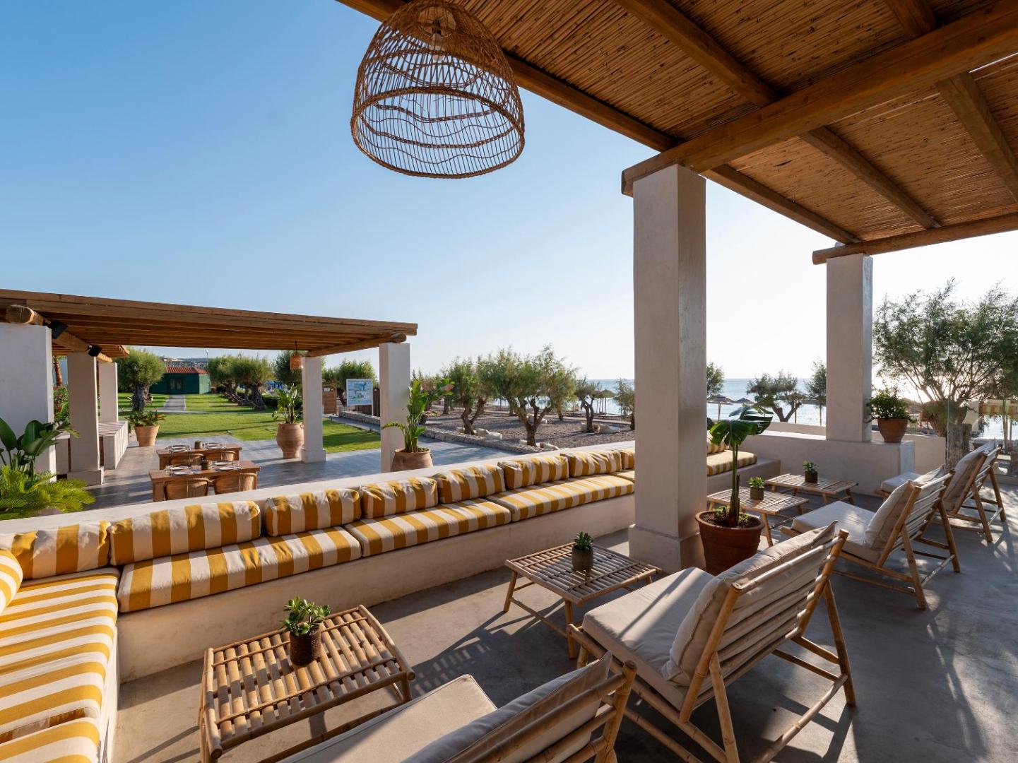 Grecotel Lux Me Dama Dama āra terase Rodas salā ar svītrainiem dīvāniem, bambusa mēbelēm un skatu uz dārzu un jūru