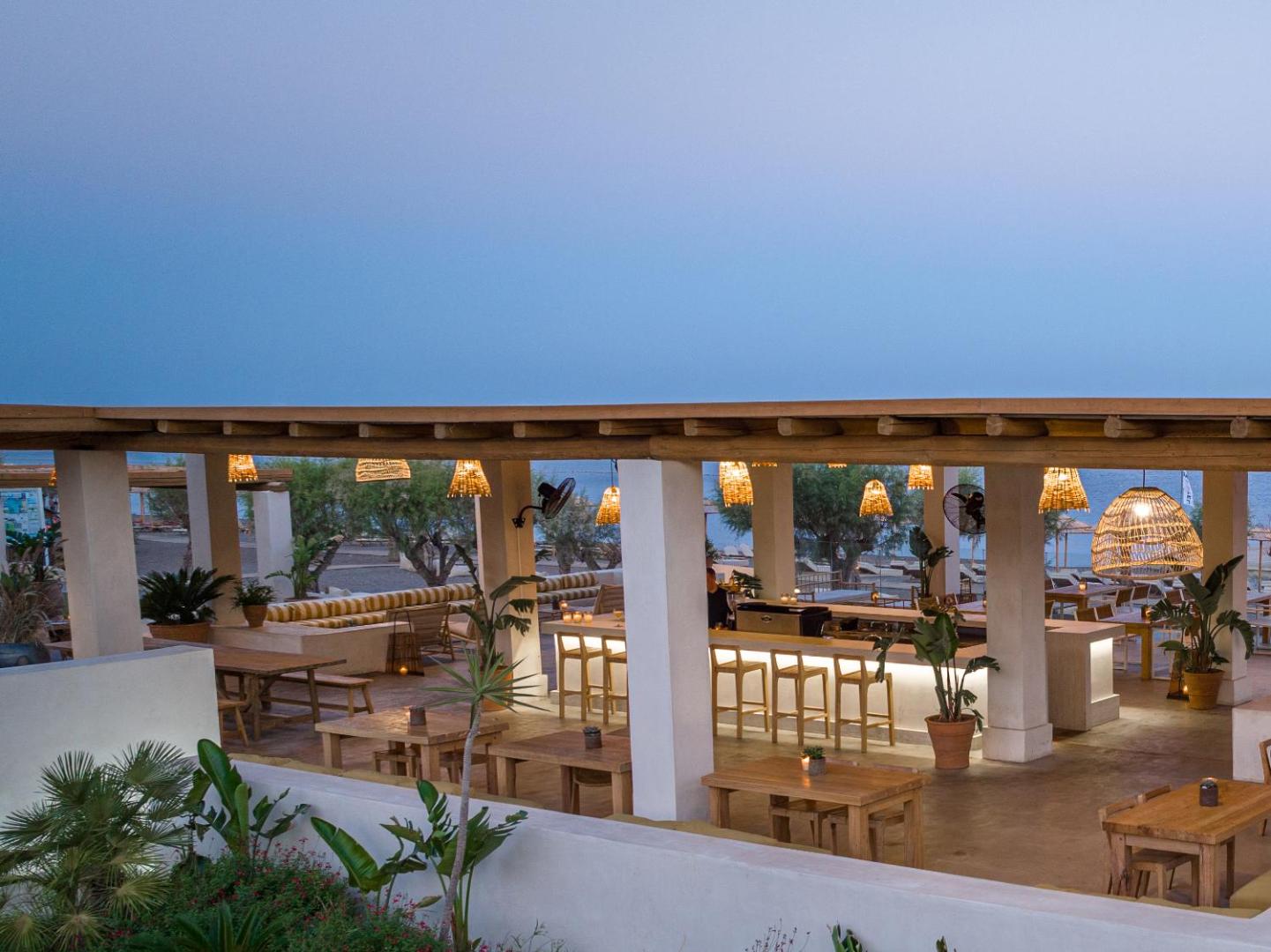 Grecotel Lux Me Dama Dama pludmales bārs un restorāns vakarā Rodas salā — mājīgs apgaismojums, koka mēbeles un skats uz jūru