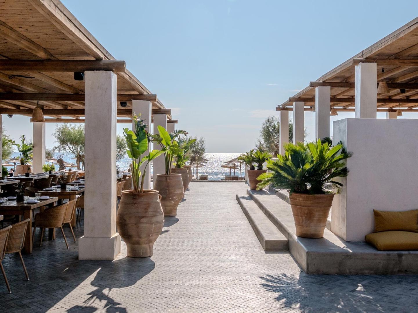 Viesnīcas Grecotel Lux Me Dama Dama āra terase ar māla vāzēm un skatu uz pludmali un saulaino jūru