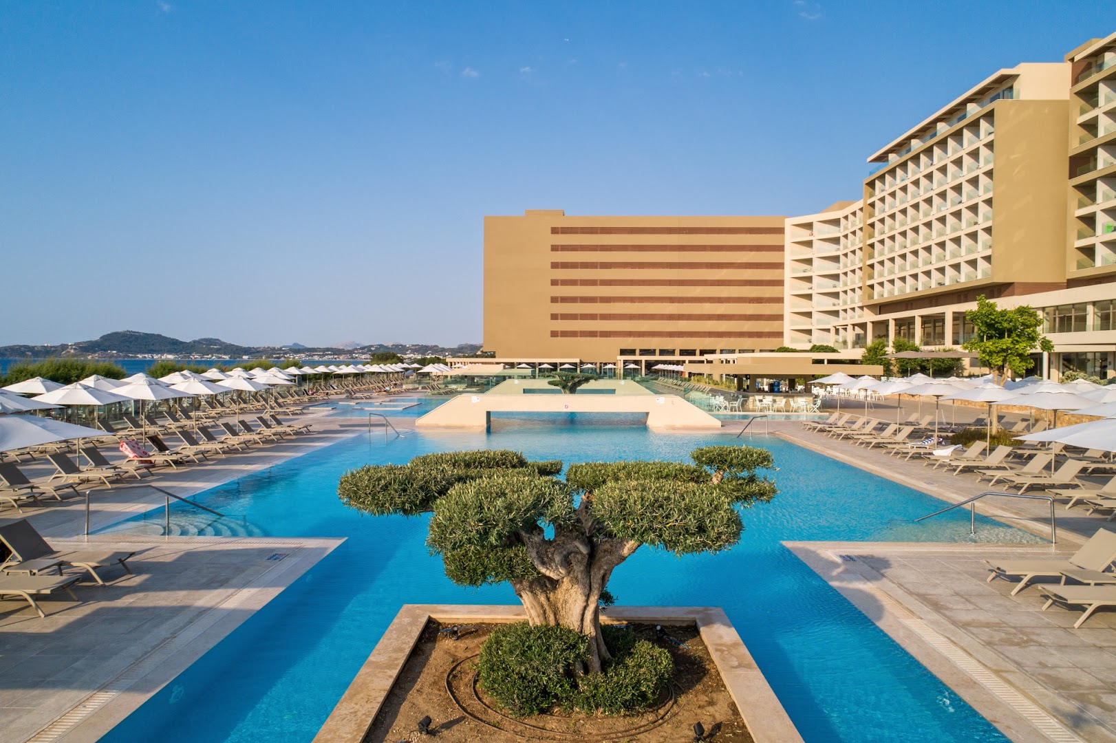 Amada Colossos Resort galvenā ēka un lielais āra baseins ar saulessargiem un olīvkoku centrā, Rodas piekrastē