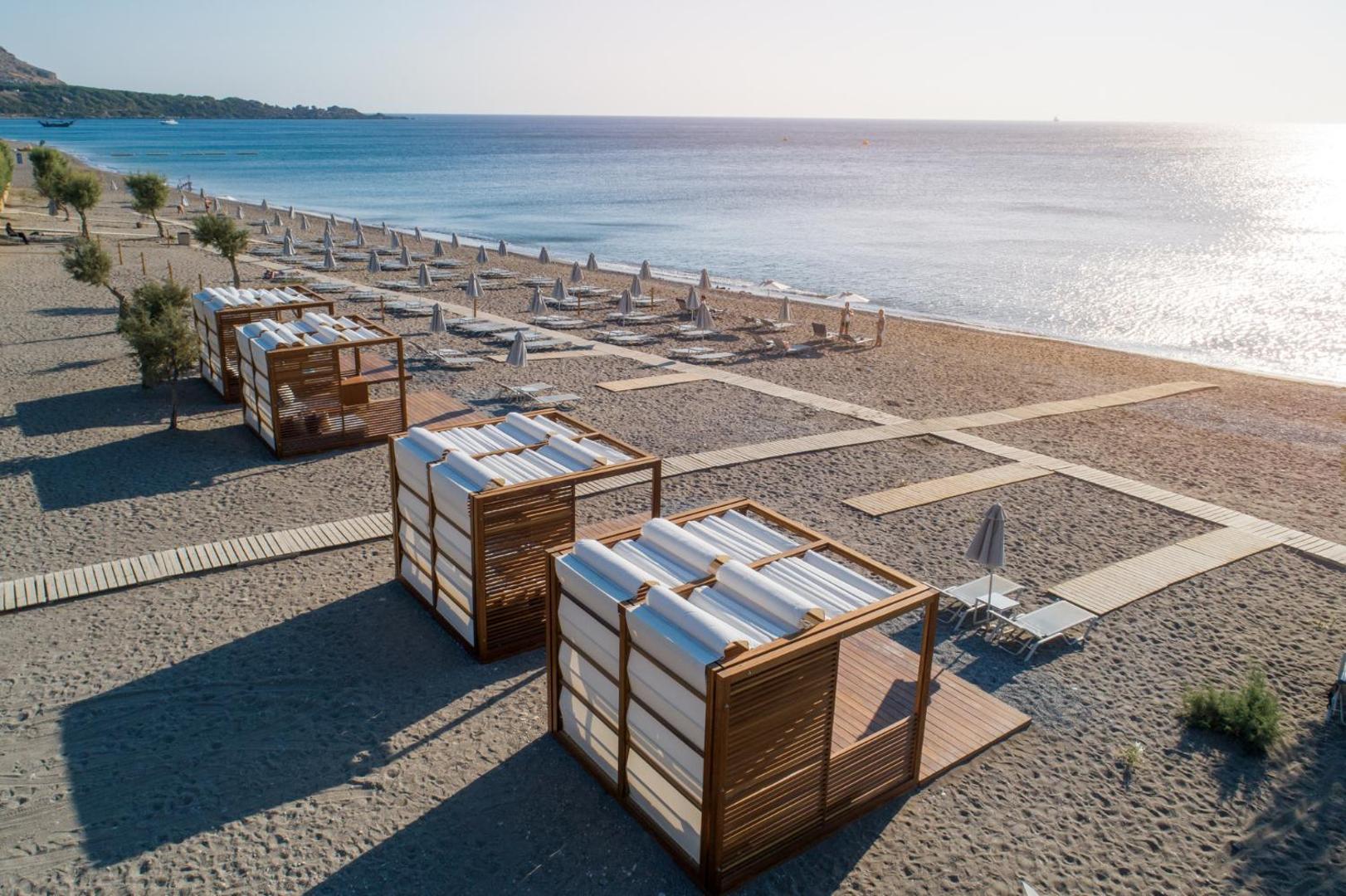 Amada Colossos Resort plašā smilšu pludmale ar koka bungalo un saulessargiem Rodas piekrastē — skats no augšas uz zilo jūru