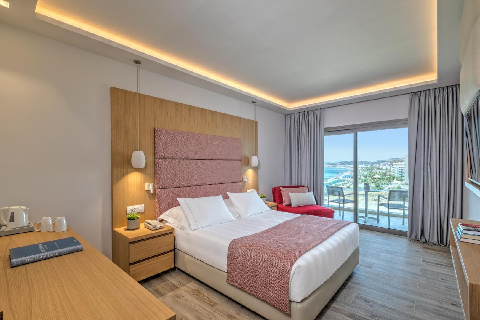 Plašs Amada Colossos Resort viesnīcas numurs ar koka apdari, ērtu gultu un izeju uz balkonu Rodas salas piekrastē