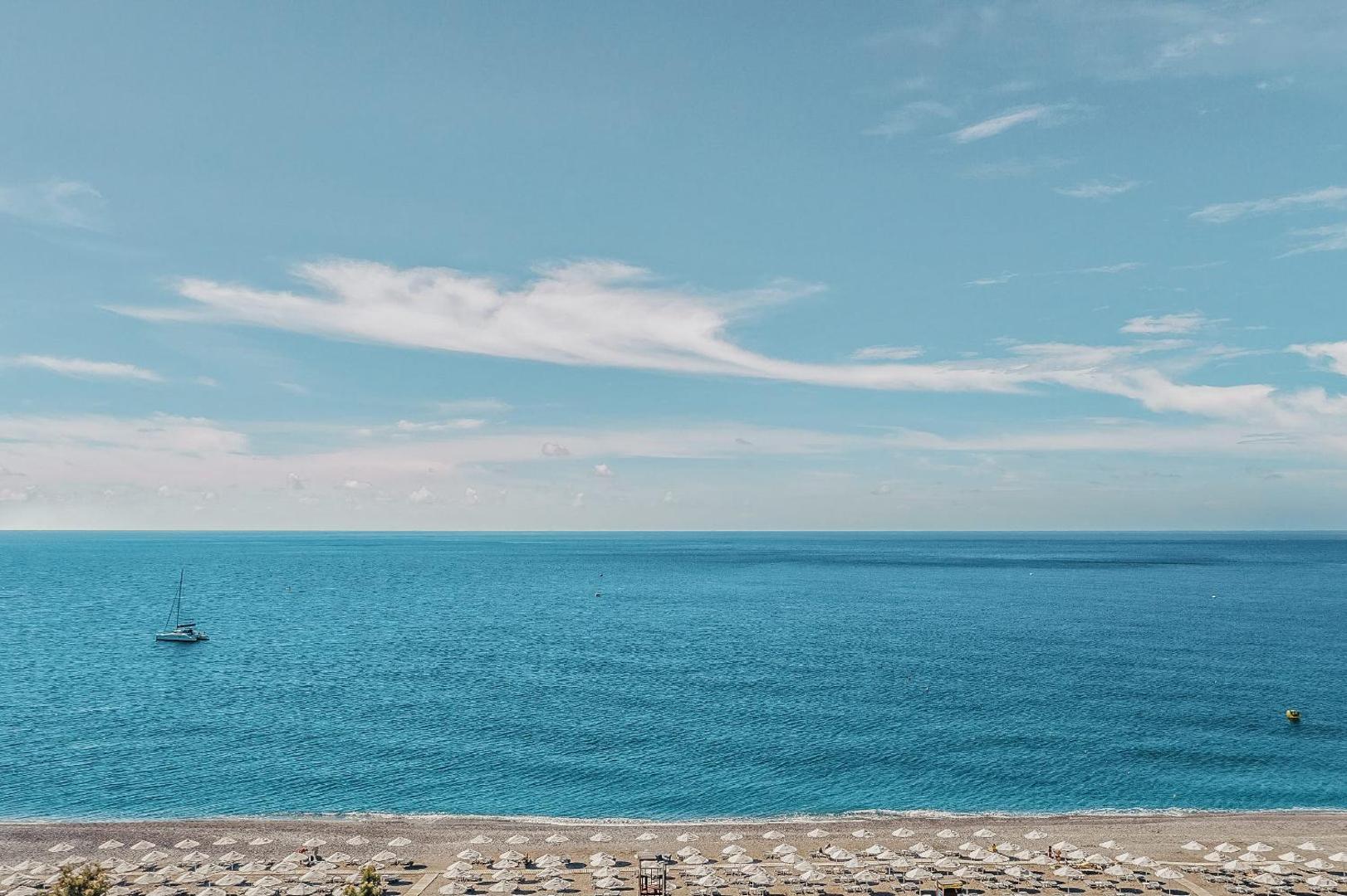 Skats uz Vidusjūru no Lindos Imperial Resort & SPA Rodas salā — gaiši zilas debesis, jahta un pludmales zona