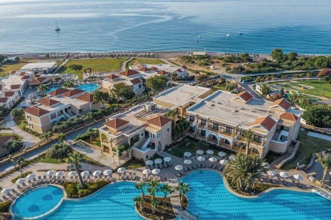 Lindos Imperial Resort & SPA numuru korpusi un baseini Rodas salā — skats no augšas uz arhitektūru un dārziem piekrastē