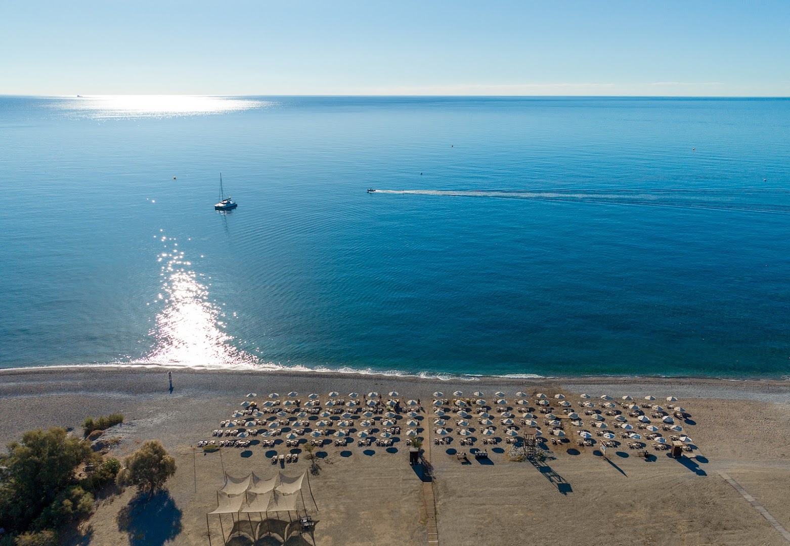 Lindos Imperial Resort & SPA privātā oļu pludmale Rodas salā — skats no augšas uz zilo jūru, jahtu un saulessargiem