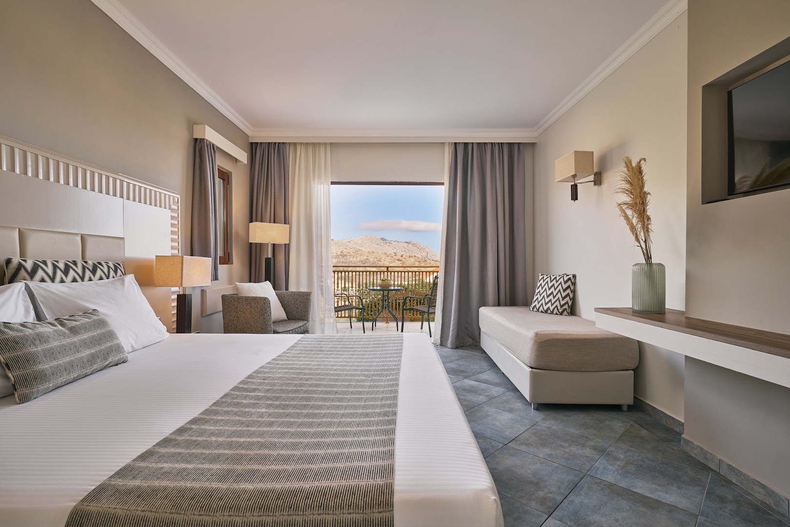 Lindos Imperial Resort & SPA moderns numurs ar divguļamo gultu, dīvānu un balkonu, no kura paveras skats uz Rodas kalniem.