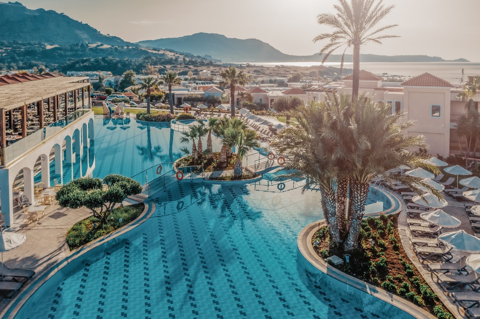 Lindos Imperial Resort & SPA plašā teritorija ar lielu baseinu, palmām un kalnu fonu saulrieta gaismā Kiotari, Rodā.