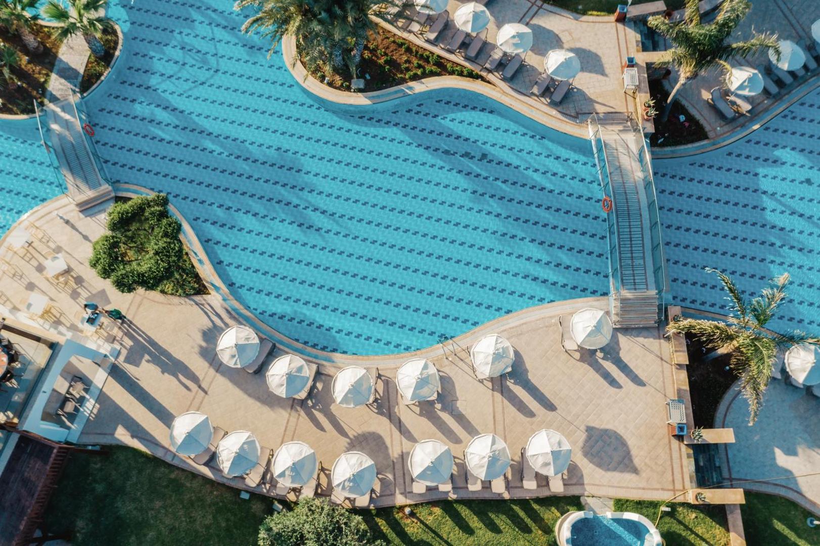 Lindos Imperial Resort & SPA baseina skats no augšas ar tiltiņu, saulessargiem un atpūtas zonu Rodas salas kūrortā.