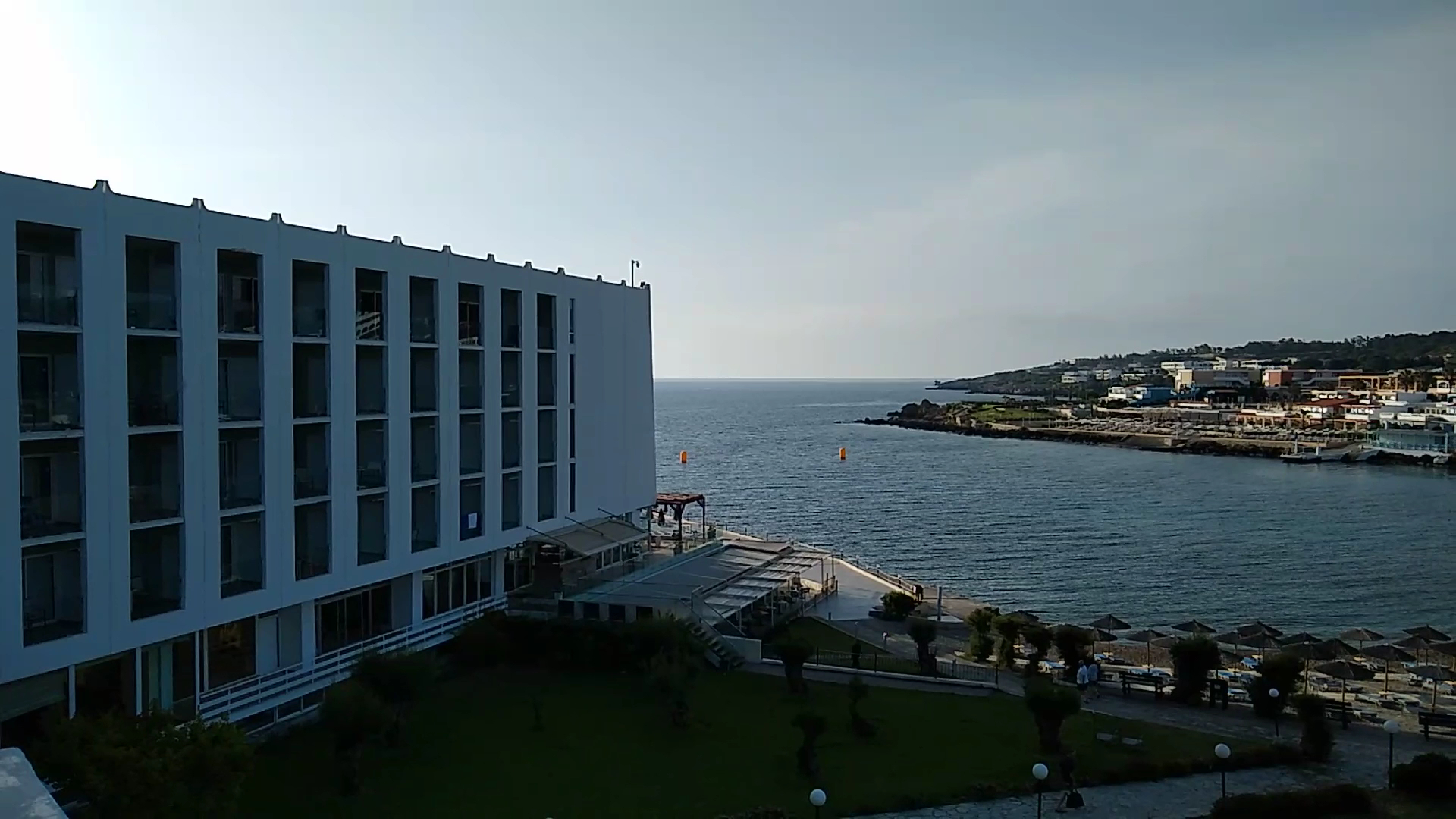 Skats no Eden Roc Resort terases uz jūras līci un piekrasti — viesnīcas korpuss un labiekārtota zaļā zona