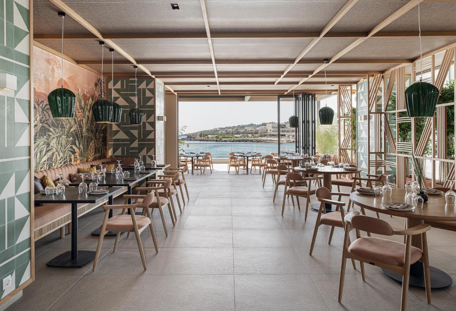 Eden Roc Resort moderns iekštelpu restorāns ar panorāmas skatu uz Vidusjūru, dizaina mēbelēm un tropu motīvu sienas dekoru