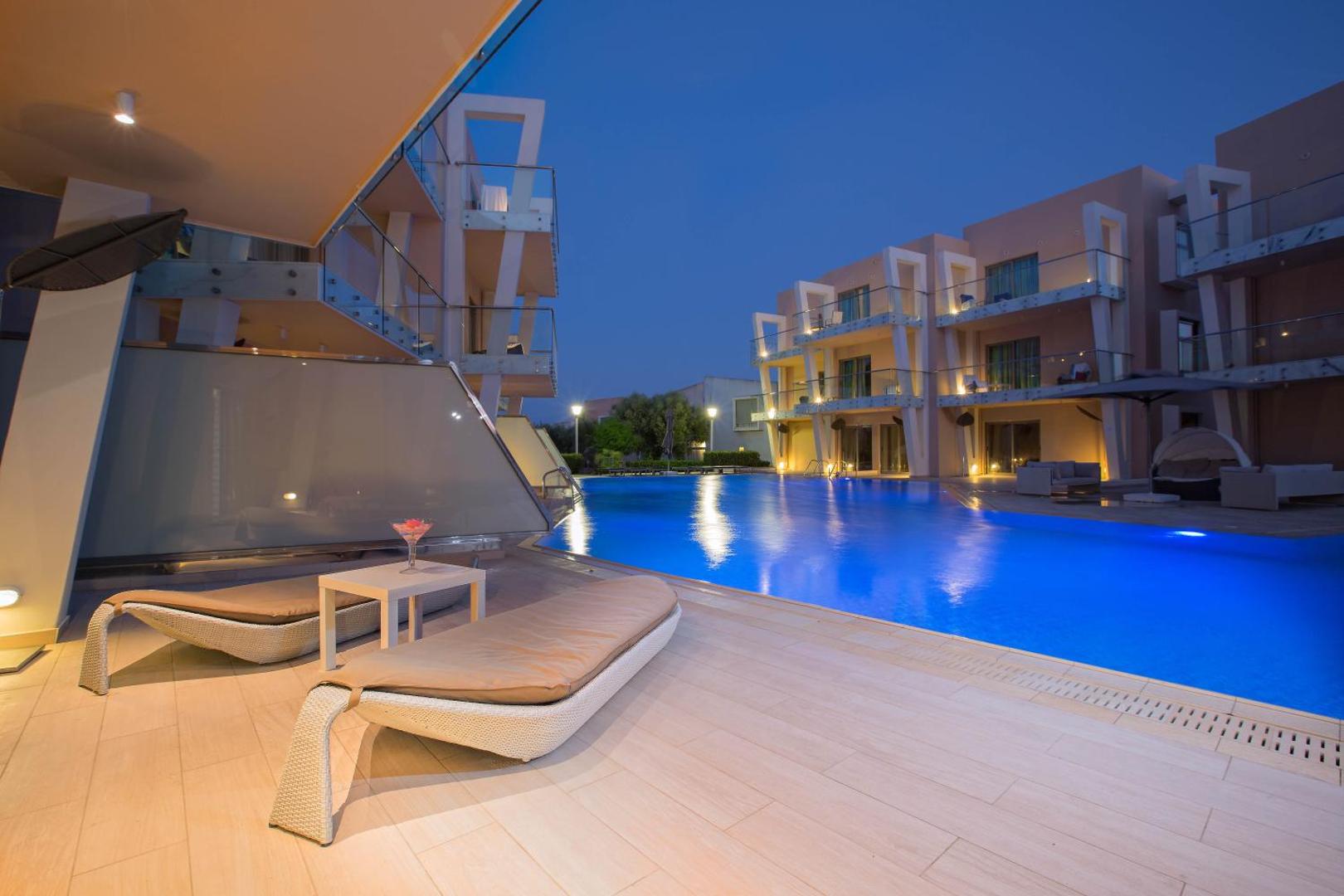 Eden Roc Resort numurs ar tiešu piekļuvi baseinam vakara apgaismojumā Rodas salā — terase ar atpūtas krēsliem un modernu arhitektūru