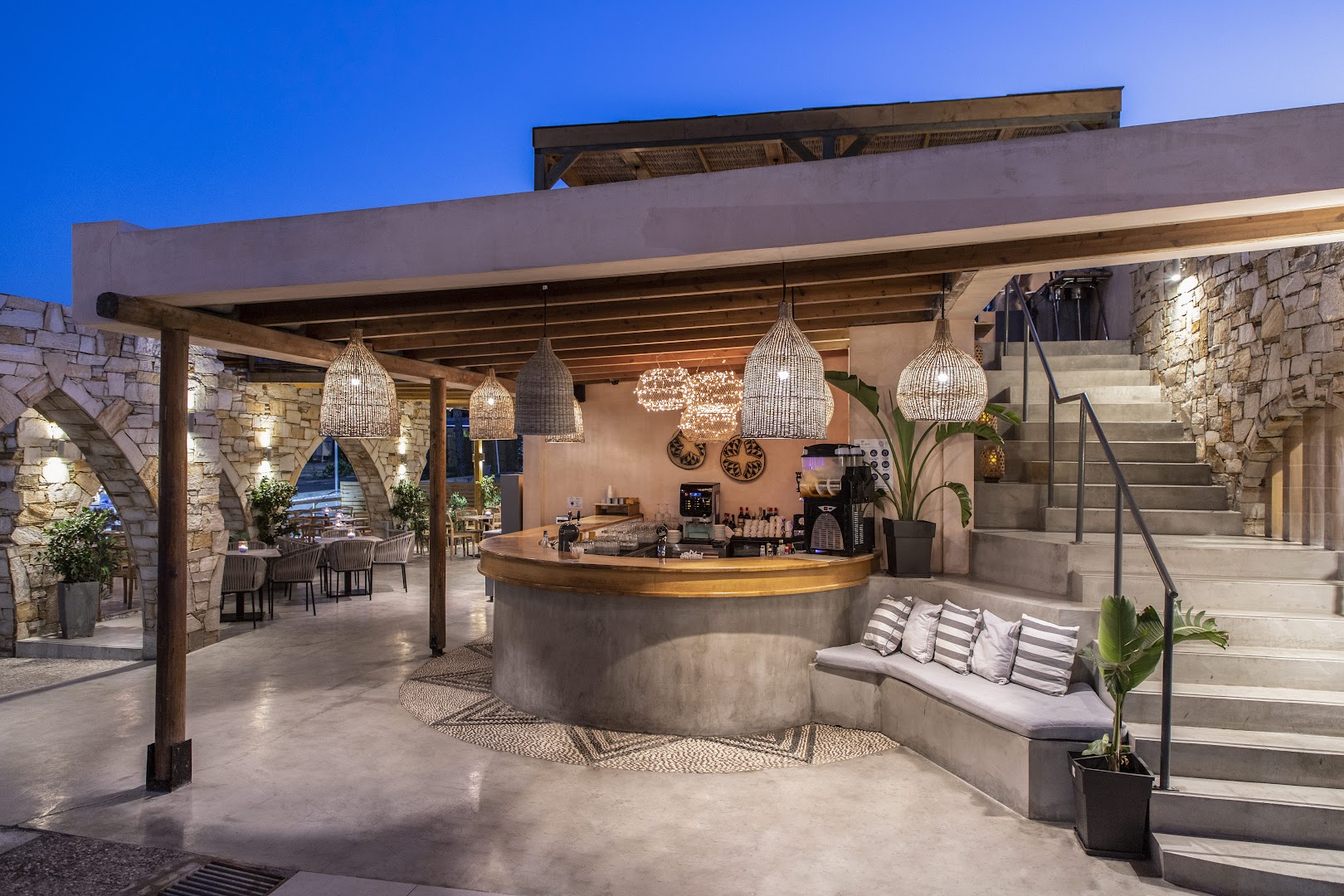 Eden Roc Resort āra bārs vakarā ar akmens arkām, siltu apgaismojumu, pītiem gaismekļiem un ērtām sēdvietām pie kāpnēm