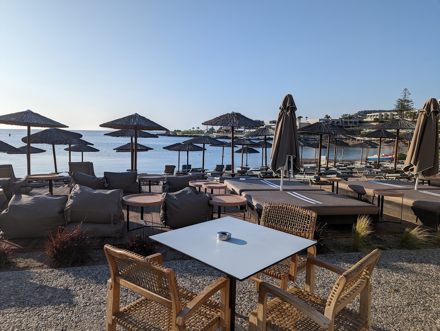 Eden Roc Resort pludmales atpūtas zona Rodas salā ar saulessargiem, ērtiem sēžammaisiem un skatu uz Egejas jūru saulainā dienā
