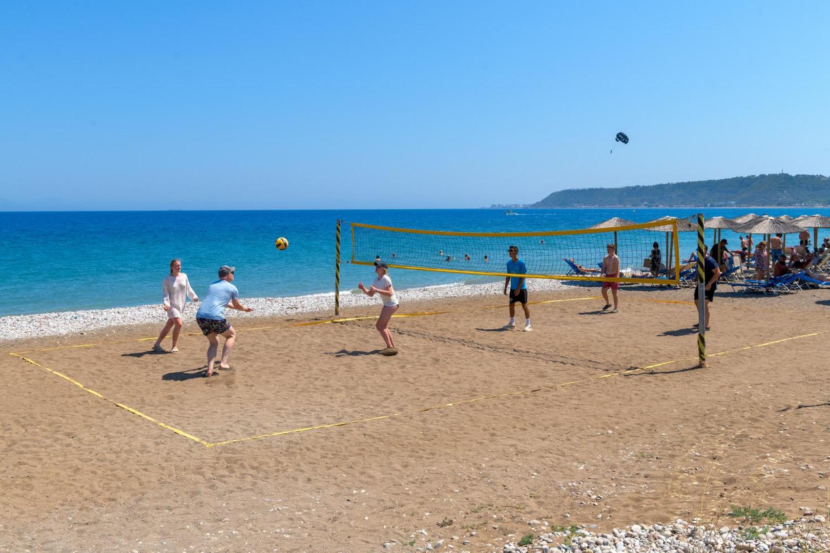 Viesi spēlē pludmales volejbolu Avra Beach Resort smilšu pludmalē pie dzidri zilās jūras saulainā dienā Rodas salā