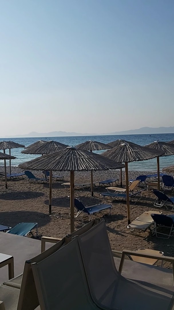 Avra Beach Resort privātā pludmale ar saulessargiem un zviļņiem Rodas salā — skats uz Egejas jūru un kalniem tālumā