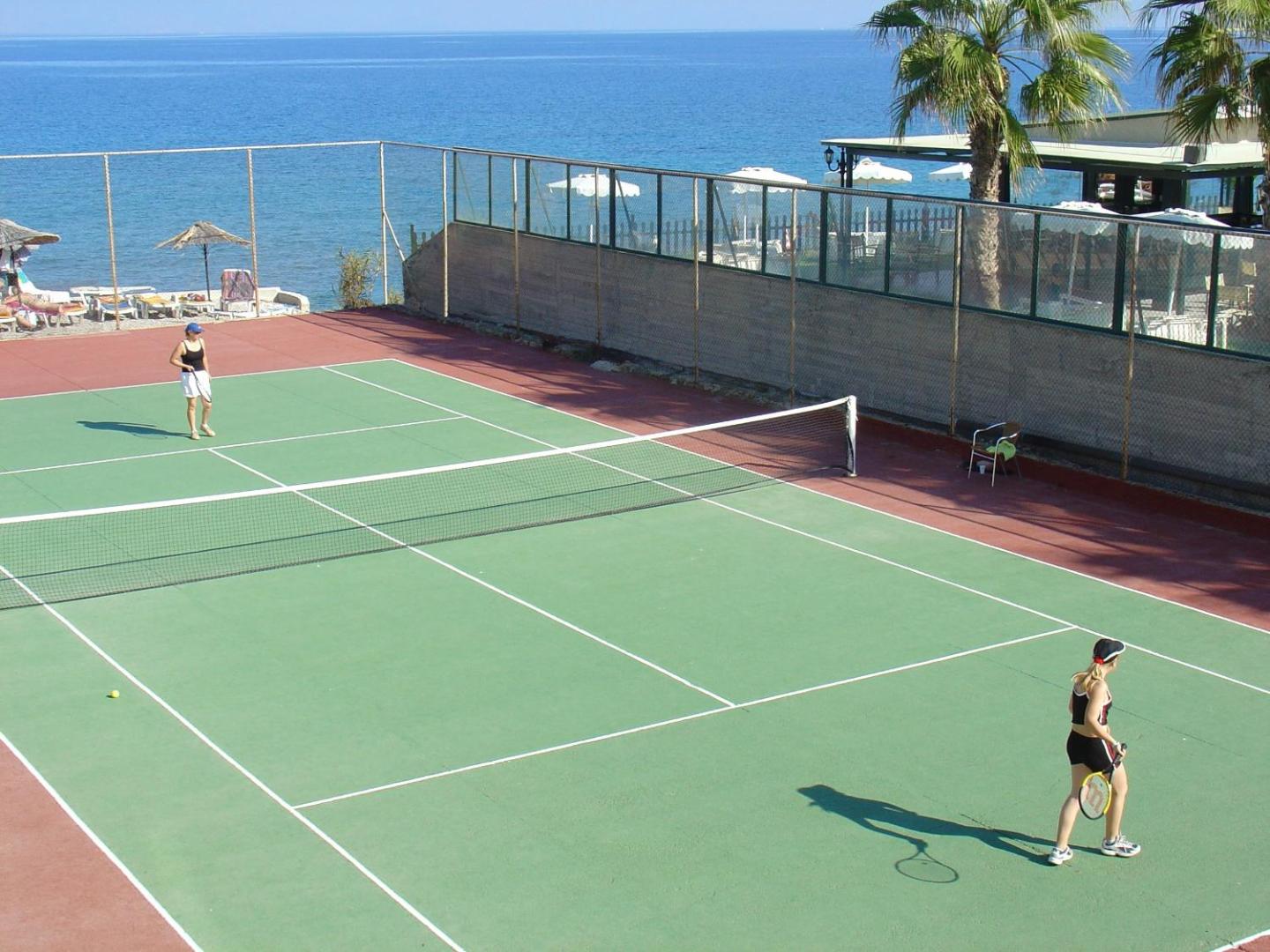 Avra Beach Resort Hotel & Bungalows tenisa korts Rodas piekrastē ar skatu uz jūru — divas sievietes spēlē tenisu saulainā dienā
