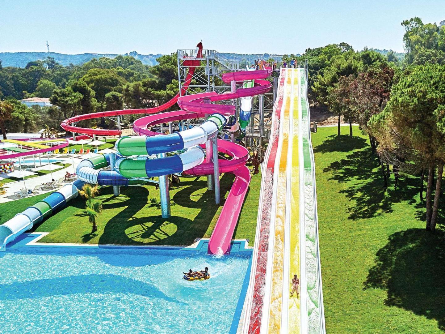 Grecotel LUXME Oasis at Riviera Olympia akvaparks ar krāsainiem ūdens slidkalniņiem, baseinu un zaļu teritoriju Peloponēsas piekrastē.