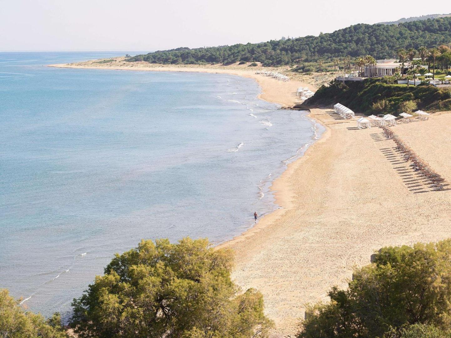 Grecotel LUXME Oasis at Riviera Olympia kūrorta plašā smilšu pludmale Peloponēsas piekrastē ar saulessargiem un tirkīzzilu jūras ūdeni