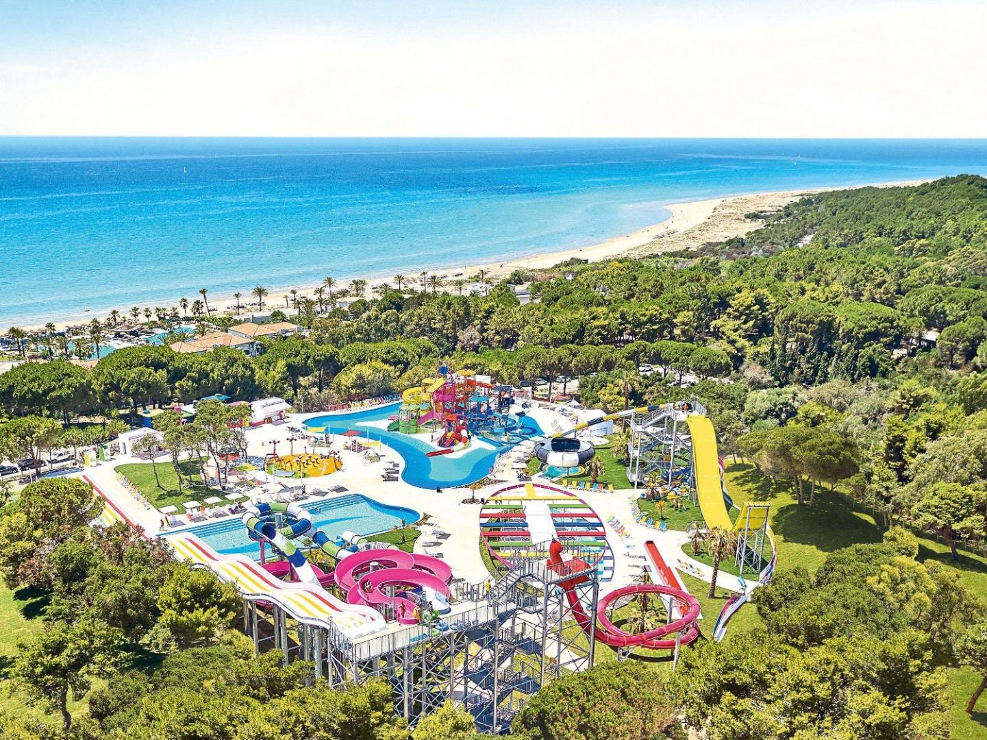 Grecotel LUXME Oasis at Riviera Olympia milzīgais akvaparks ar krāsainiem slidkalniņiem, ko ieskauj priežu mežs pie jūras.