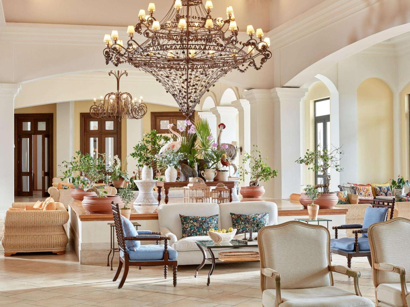 Grecotel LUXME Oasis at Riviera Olympia greznais vestibils ar lielu lustru, gaišiem dīvāniem, dekoratīviem augiem un klasisku interjeru.