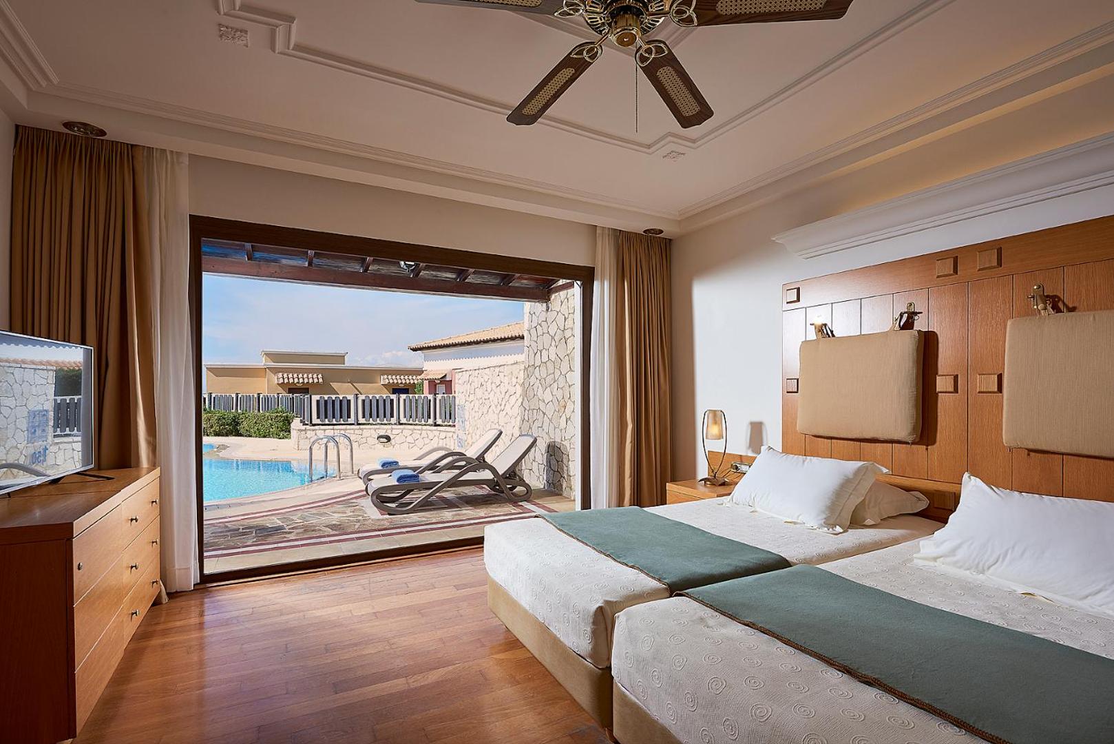 Aldemar Olympian Village numurs ar koka mēbelēm un izeju uz terasi pie baseina Grieķijas kūrortā.