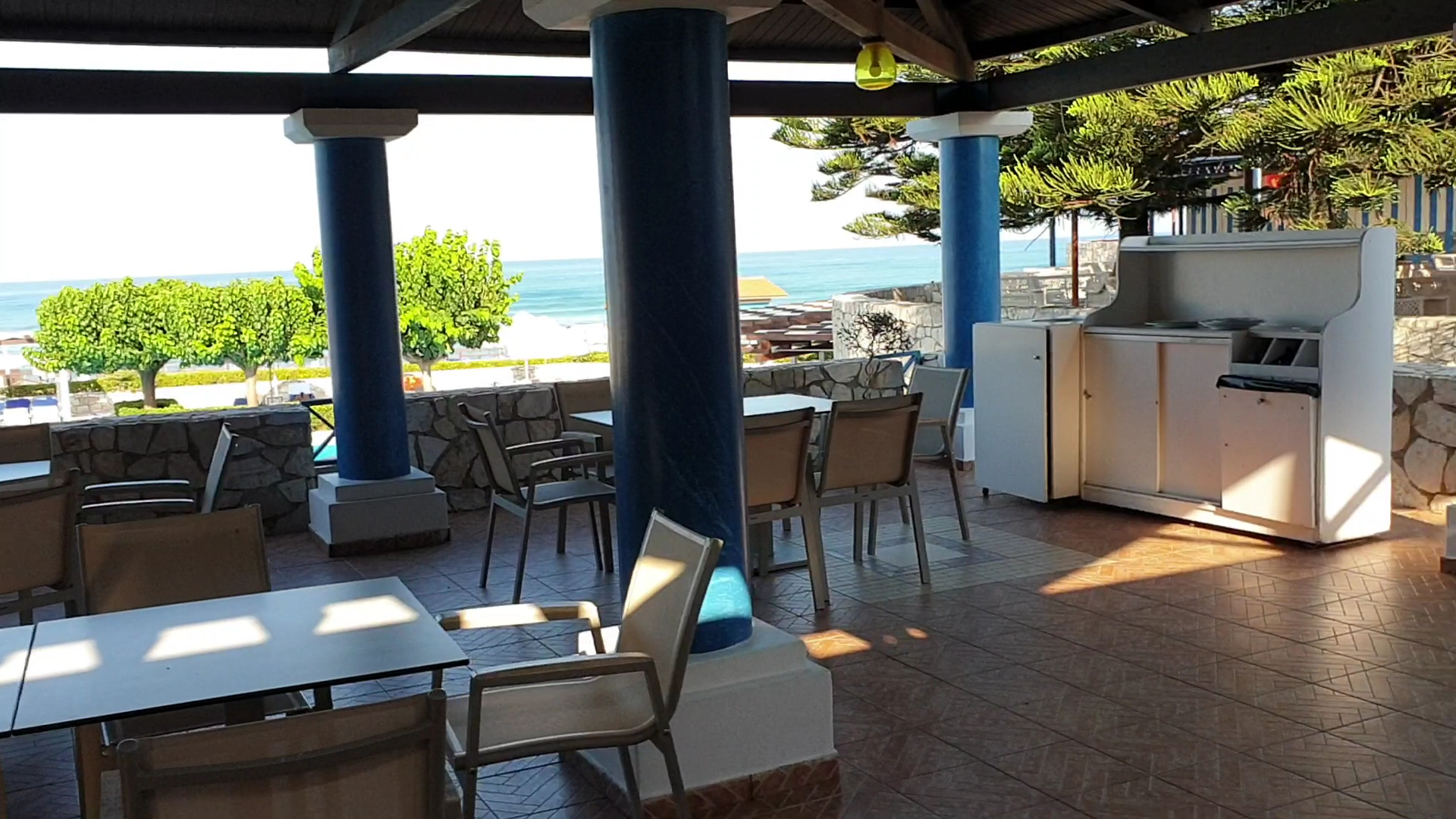 Aldemar Olympian Village āra bāra zona ar zilām kolonnām un galdiņiem zem nojumes, skats uz dārzu un jūru