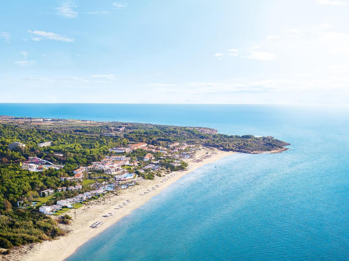 Aerofoto skats uz Grecotel Ilia Palms & Aqua Park kūrortu Peloponēsā — gara smilšu pludmale un dzidri zils Jonijas jūras ūdens.
