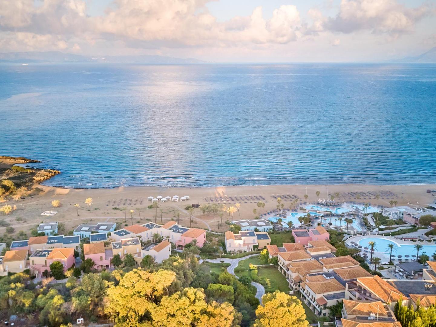 Grecotel Ilia Palms & Aqua Park viesnīcas komplekss un bungalo Peloponēsas piekrastē — skats no augšas uz baseiniem un smilšu pludmali.