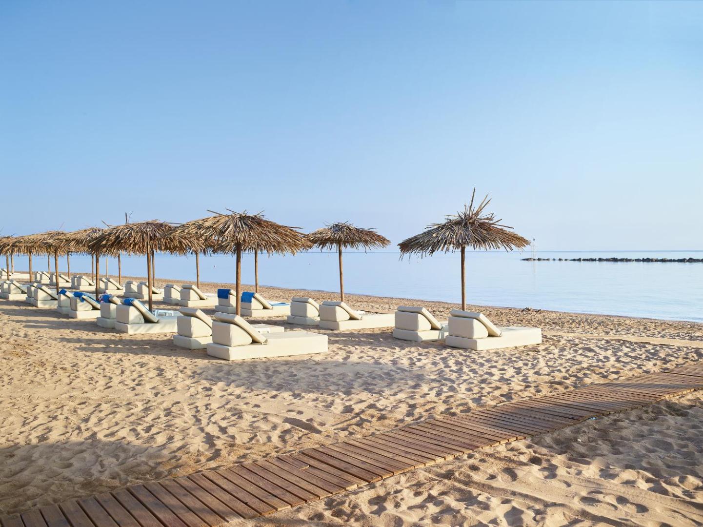 Grecotel Casa Marron pludmales zona ar koka laipām, salmu saulessargiem un ērtiem sauļošanās krēsliem Peloponēsas piekrastē Grieķijā