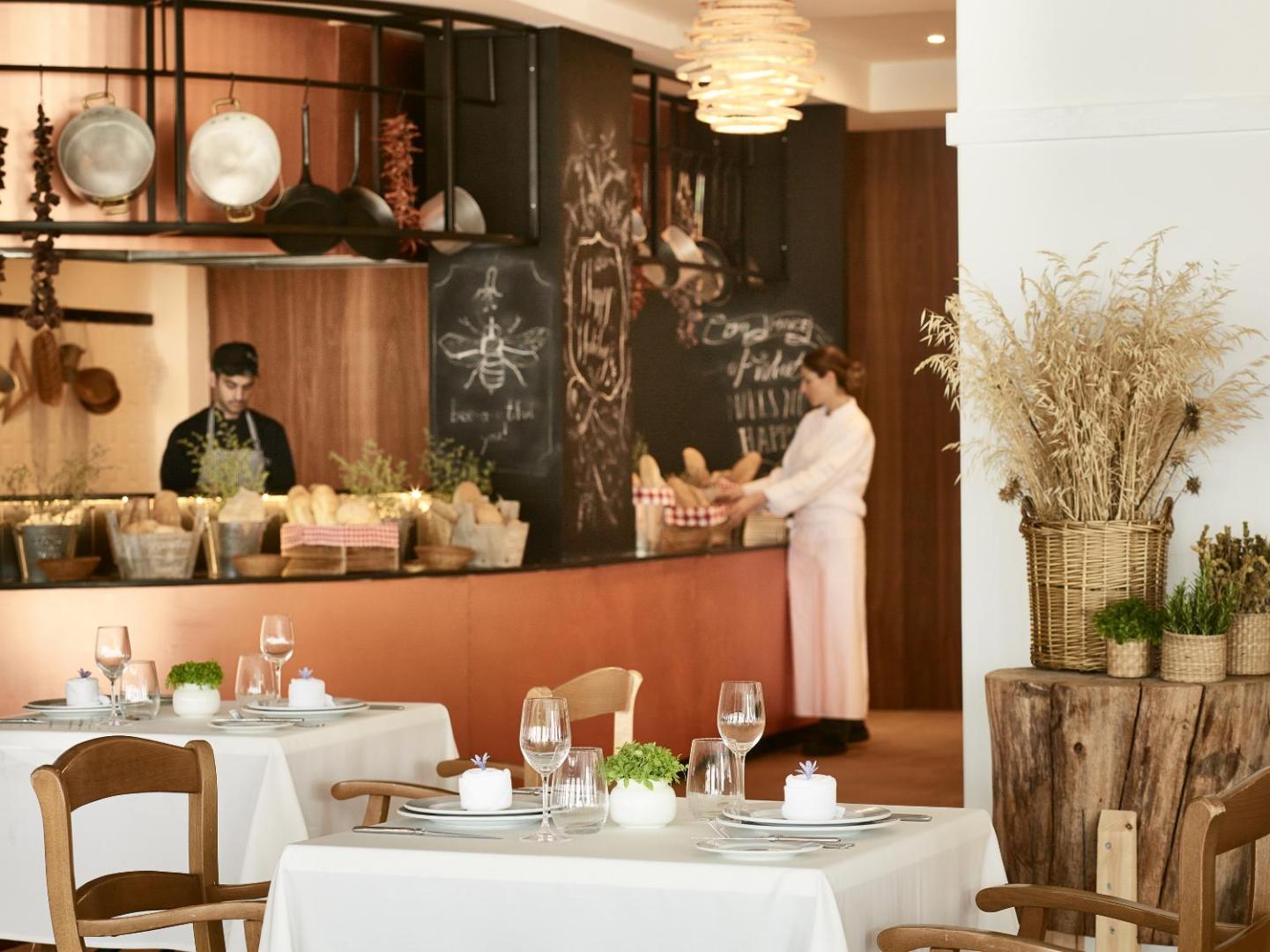 Grecotel Casa Marron restorāna interjers ar atvērto virtuvi un klātiem galdiem Lakopetrā, Peloponēsā — mājīga atmosfēra ar koka elementiem