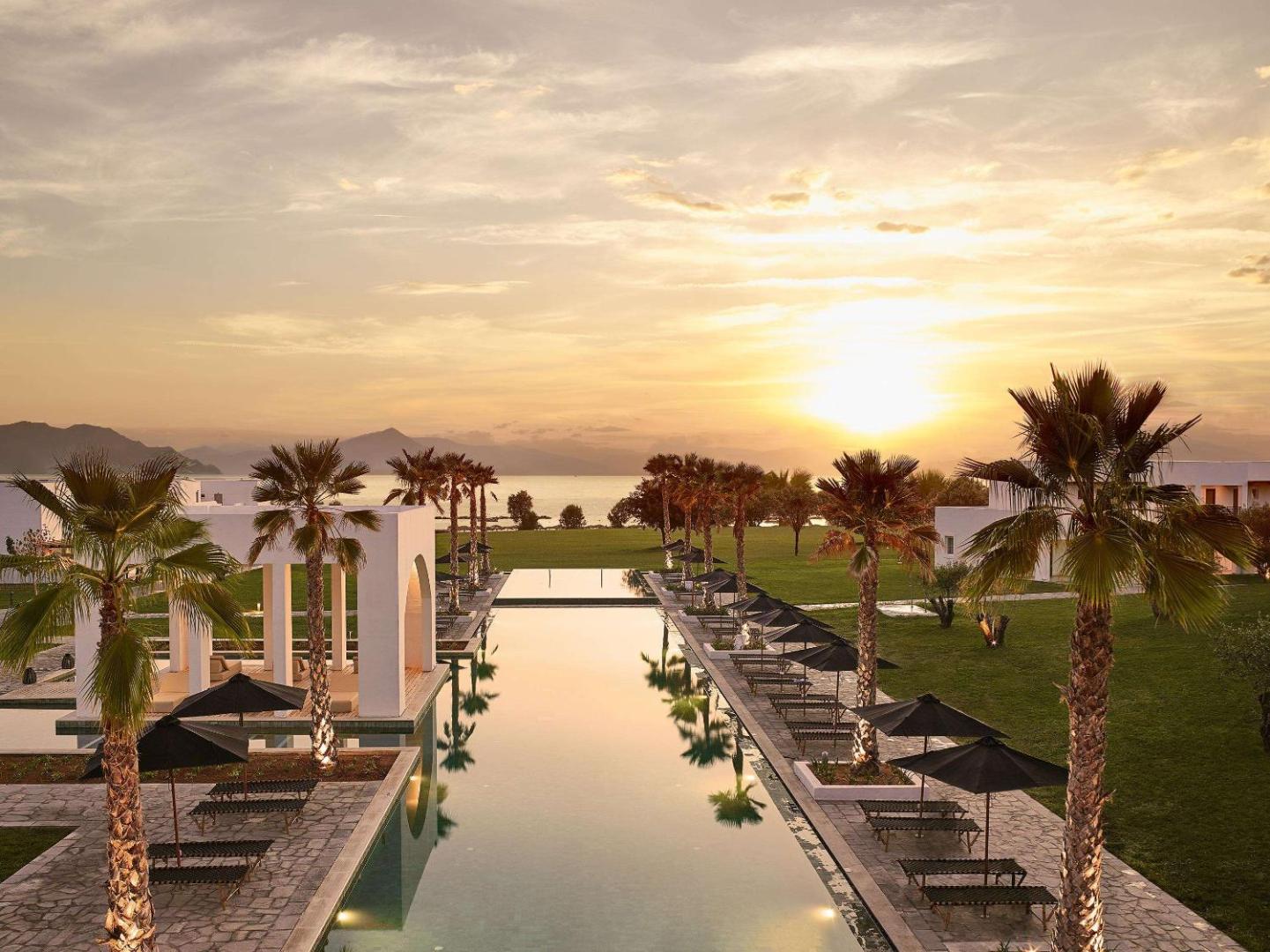 Grecotel Casa Marron āra baseins saulrietā Peloponēsā — skats uz jūru, palmām un sauļošanās krēsliem pie izgaismota baseina