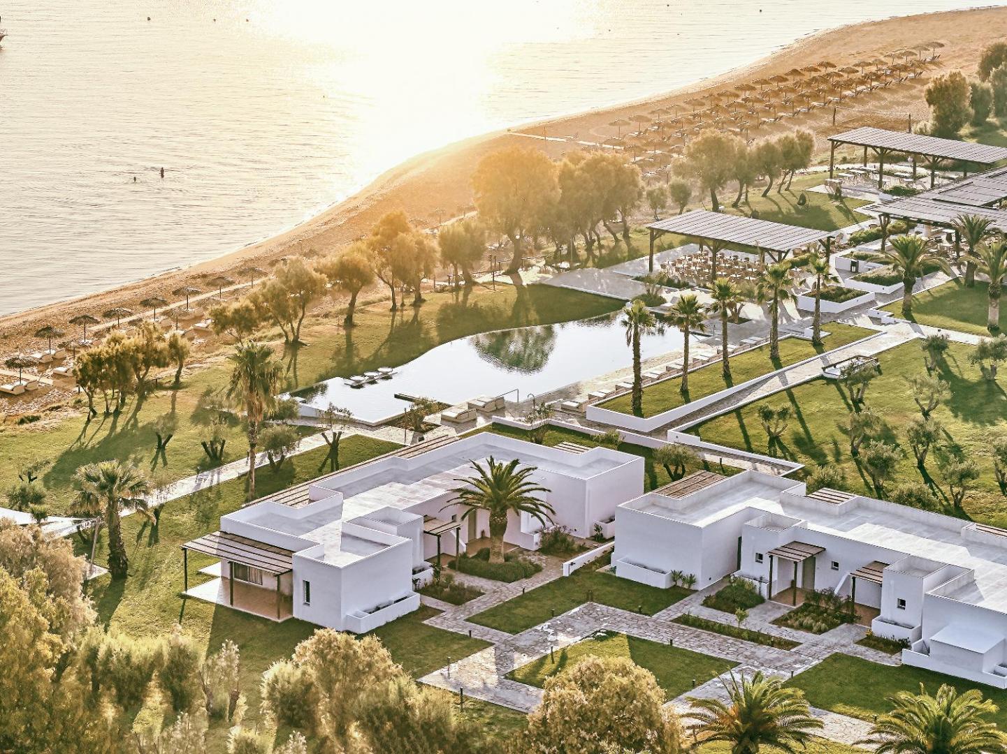 Grecotel Casa Marron kūrorta skats no augšas uz bungalo tipa numuriem, baseinu un pludmali saulrietā Peloponēsas piekrastē
