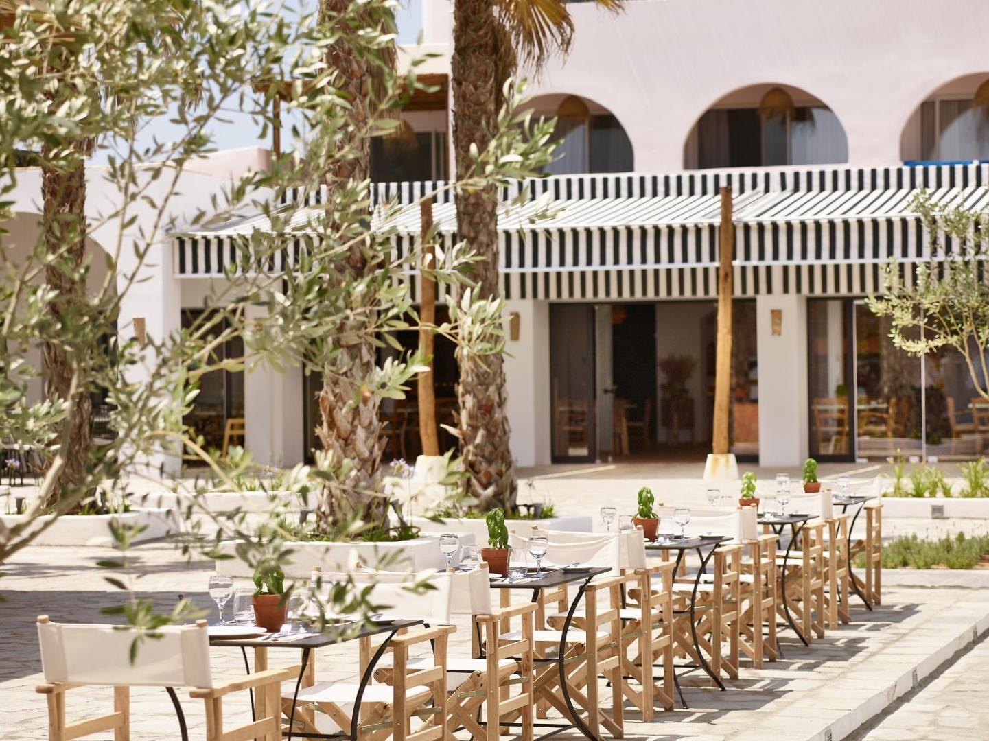 Grecotel Casa Marron viesnīcas pagalms ar āra galdiņiem, olīvkokiem un tradicionālu grieķu arhitektūru Peloponēsas reģionā