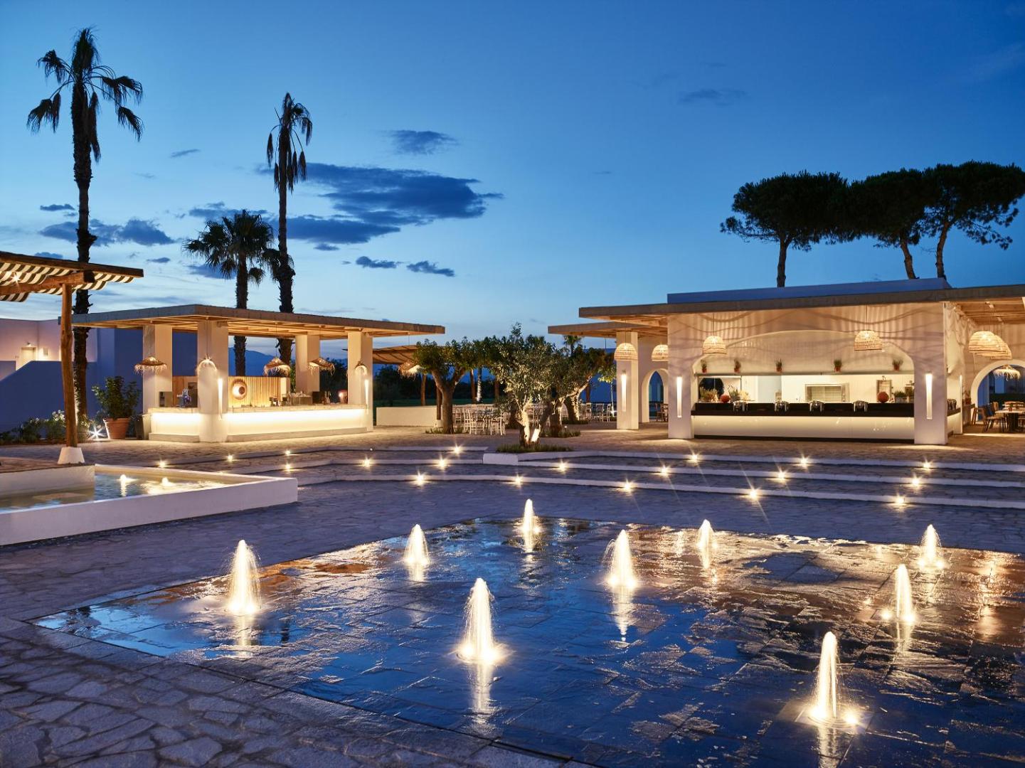 Grecotel Casa Marron vakara apgaismojums pie strūklakām un āra bāra zonas ar palmām un mājīgu atmosfēru