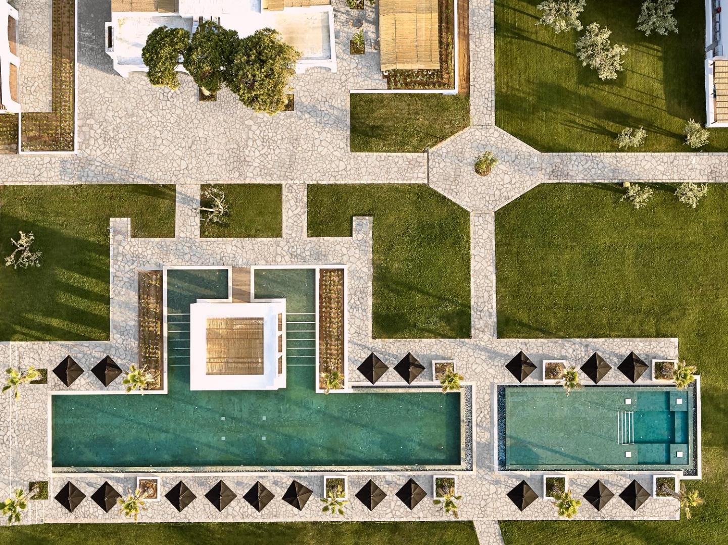 Grecotel Casa Marron dizaina baseini un kopti dārza celiņi no augšas — simetriska arhitektūra un atpūtas zonas ar saulessargiem