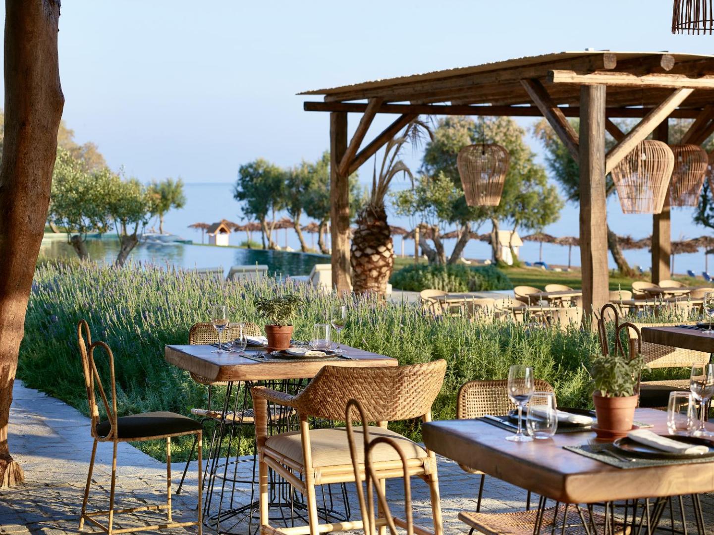 Grecotel Casa Marron restorāna terase ar koka galdiem un pītiem krēsliem, skats uz baseinu un jūru Peloponēsā