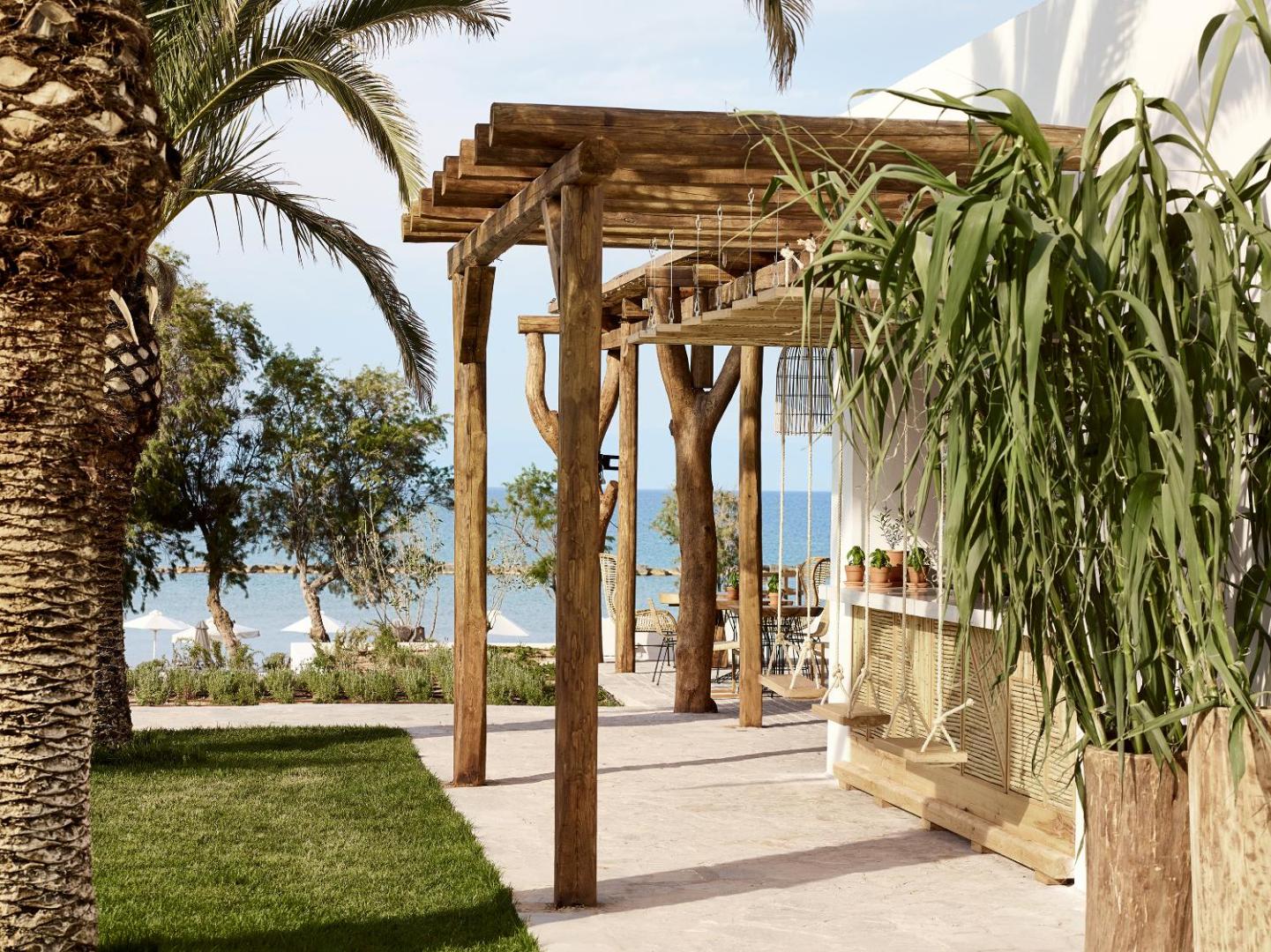 Grecotel Casa Marron āra bārs ar koka pergolu un šūpolēm pie piekrastes Peloponēsā, Grieķijā — skats uz jūru un palmām