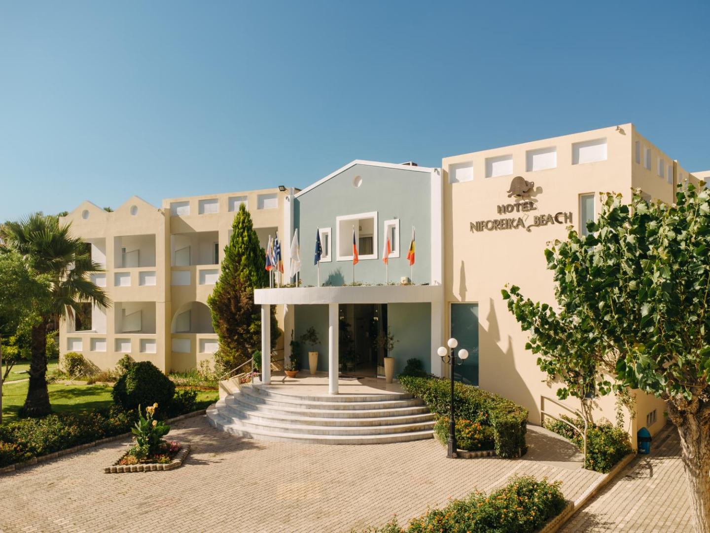 Niforeika Beach Hotel & Bungalows ieeja Peloponēsā — gaiša fasāde ar karogiem un koptu apstādījumu zonu pie galvenajām durvīm
