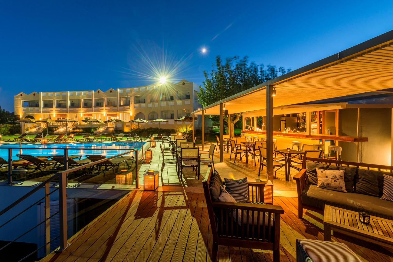 Niforeika Beach Hotel & Bungalows vakara skats uz āra baseinu un bāru ar terasi — izgaismota viesnīcas fasāde un mēbelēta atpūtas zona