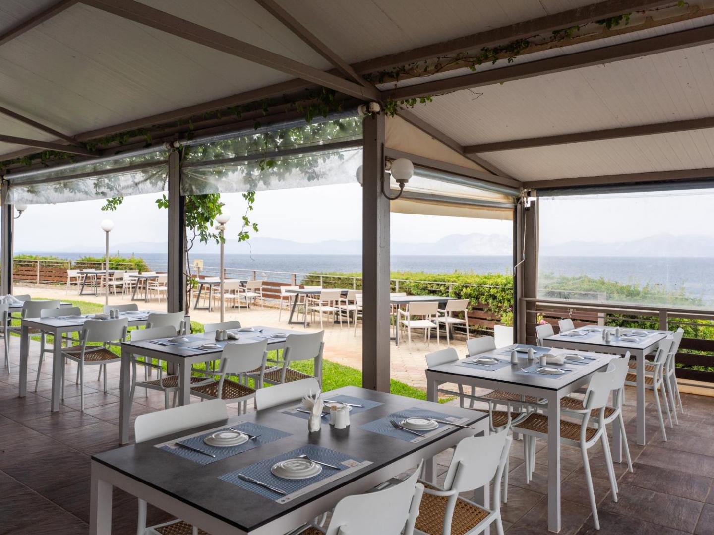 Niforeika Beach Hotel āra terases restorāns ar skatu uz jūru — balti galdi un krēsli zem nojumes piekrastē