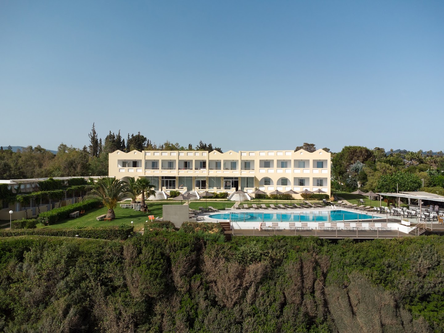 Niforeika Beach Hotel & Bungalows Peloponēsas piekrastē — skats uz galveno ēku, āra baseinu un labiekārtotu zālienu ar palmām
