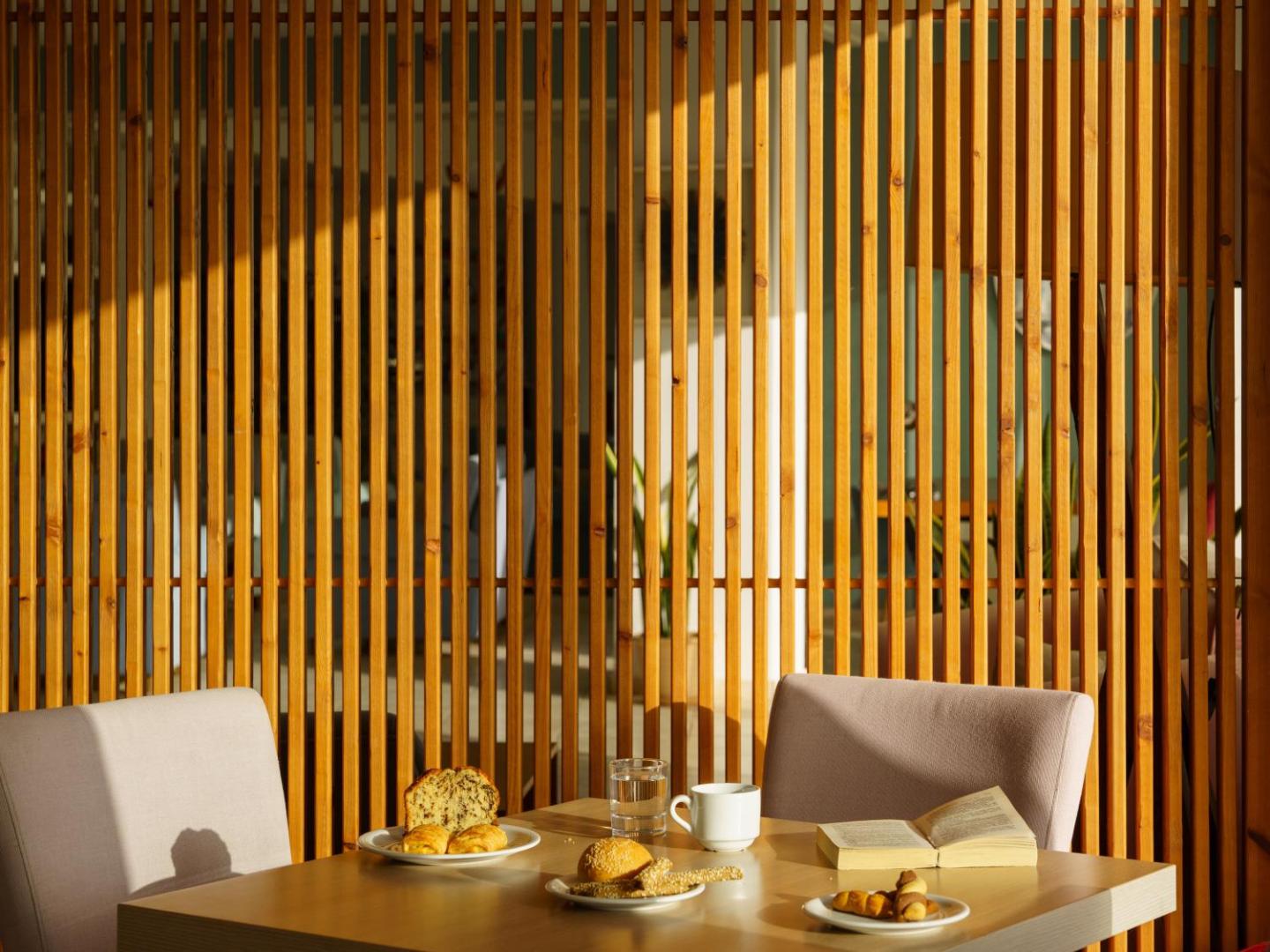 Mājīgs brokastu galds Niforeika Beach Hotel restorānā pie koka dekoratīvās sienas — kafija, smalkmaizītes un grāmata rīta saulē