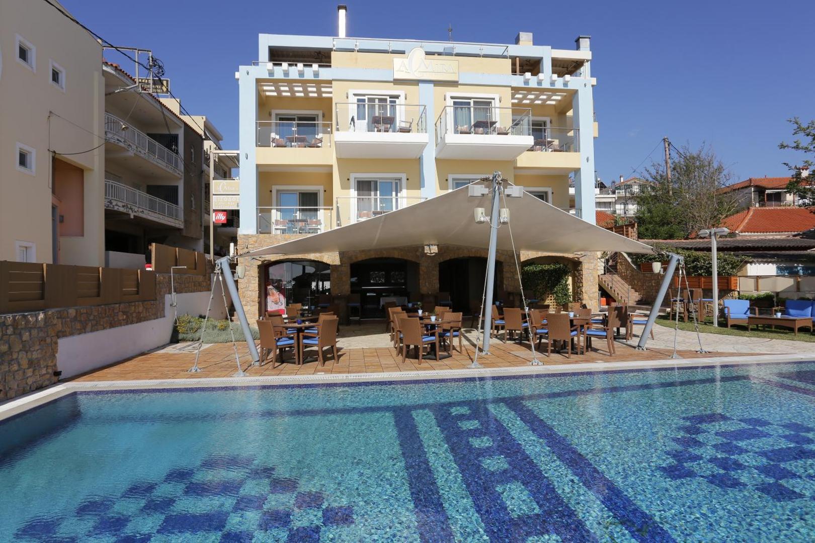 Almira Hotel Arkoudi fasāde un āra baseins ar restorāna zonu zem nojumes saulainā dienā Grieķijā