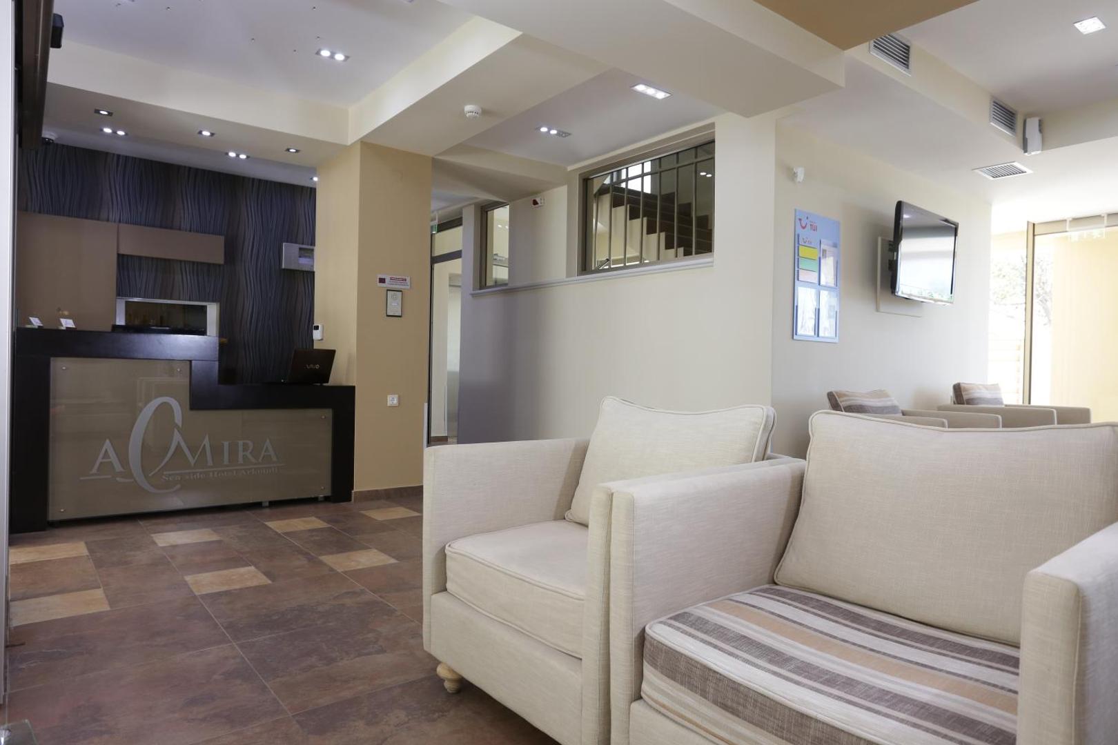 Almira Hotel Arkoudi recepcijas zona ar modernu leti un gaišiem atpūtas krēsliem viesu uzņemšanai Arkoudi ciemata piekrastē, Grieķijā.