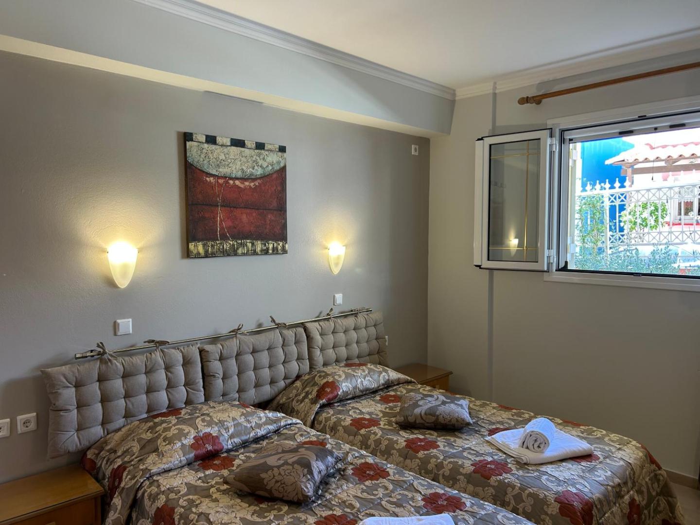 Brati II Beach Hotel gaišs numurs ar divām gultām, dekoratīviem spilveniem un gleznu pie sienas Peloponēsas reģionā Grieķijā.