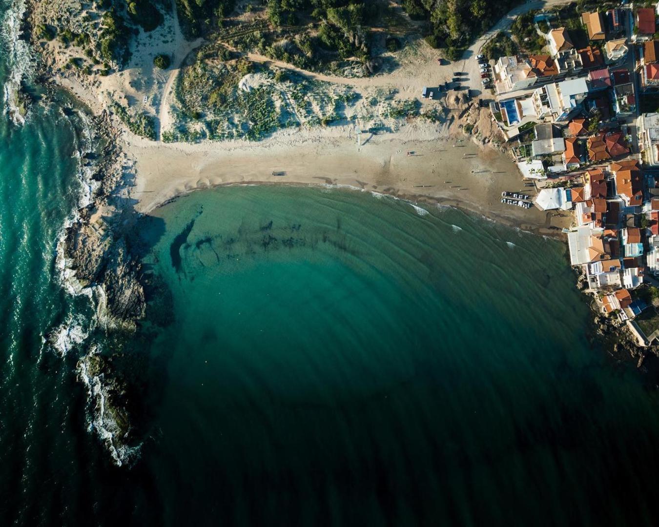 Brati II Beach Hotel apkārtnes skats no putna lidojuma uz smilšu pludmali, dzidru jūras līci un piekrastes apbūvi Peloponēsā.