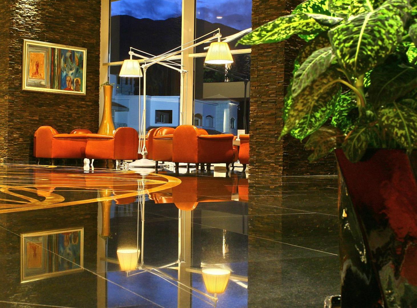 Mājīga atpūtas zona viesnīcā Splendid Conference & Spa Resort ar oranžiem atpūtas krēsliem, akmens sienu un skatu uz kalniem vakarā