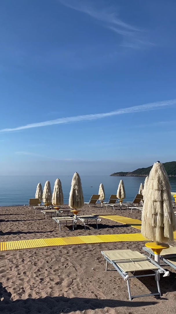 Splendid Conference & Spa Resort pludmales zona ar saulessargiem un sauļošanās krēsliem saulainā dienā — skats uz mierīgu jūras līci